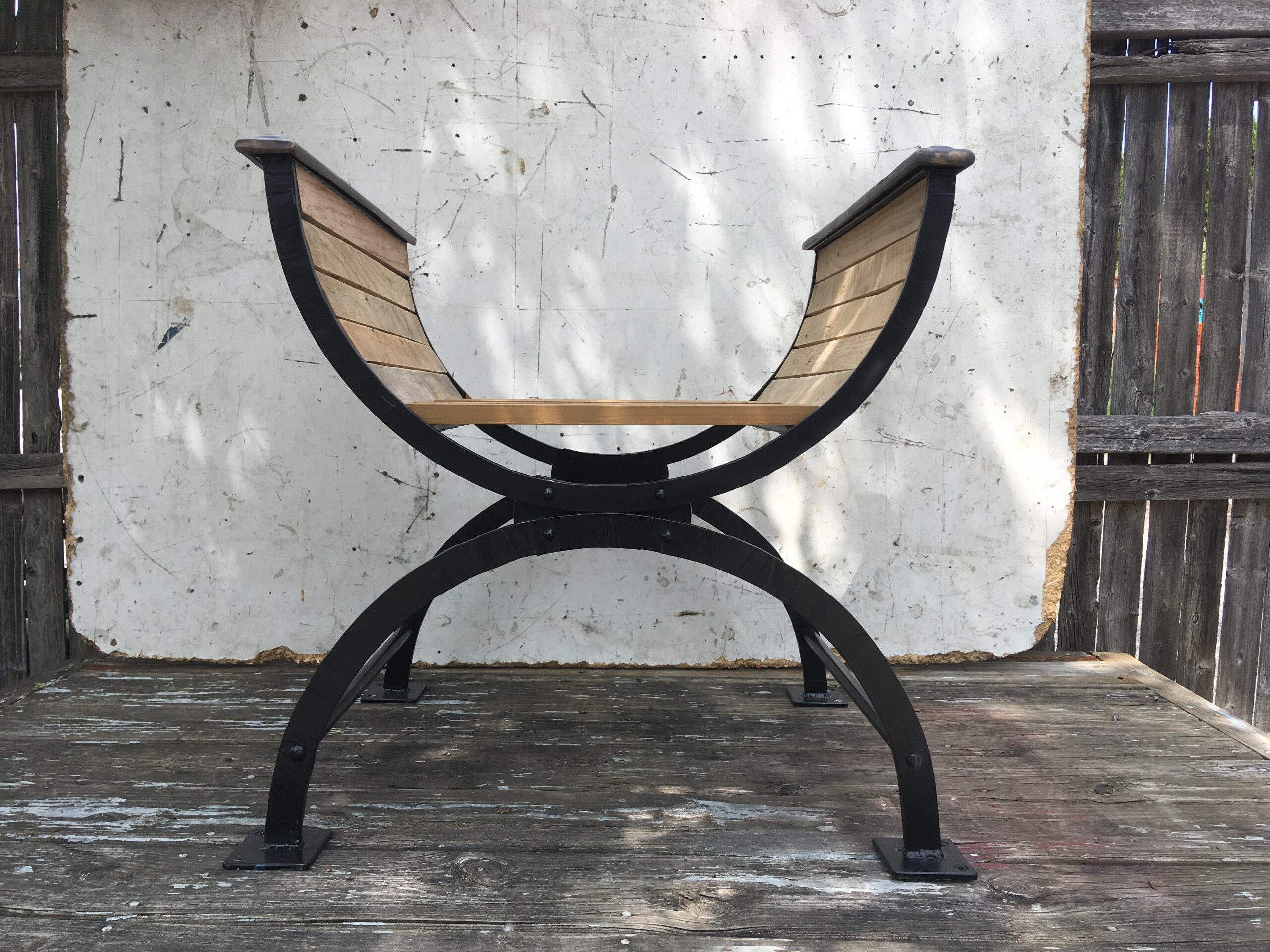 Forged black metal Roman throne with curved legs and a wood slat seat and arms