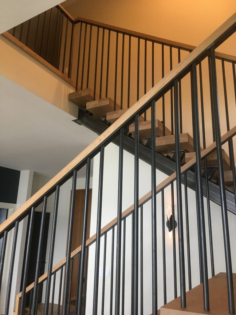 Black metal balusters with a wood cap rail along an open staircase