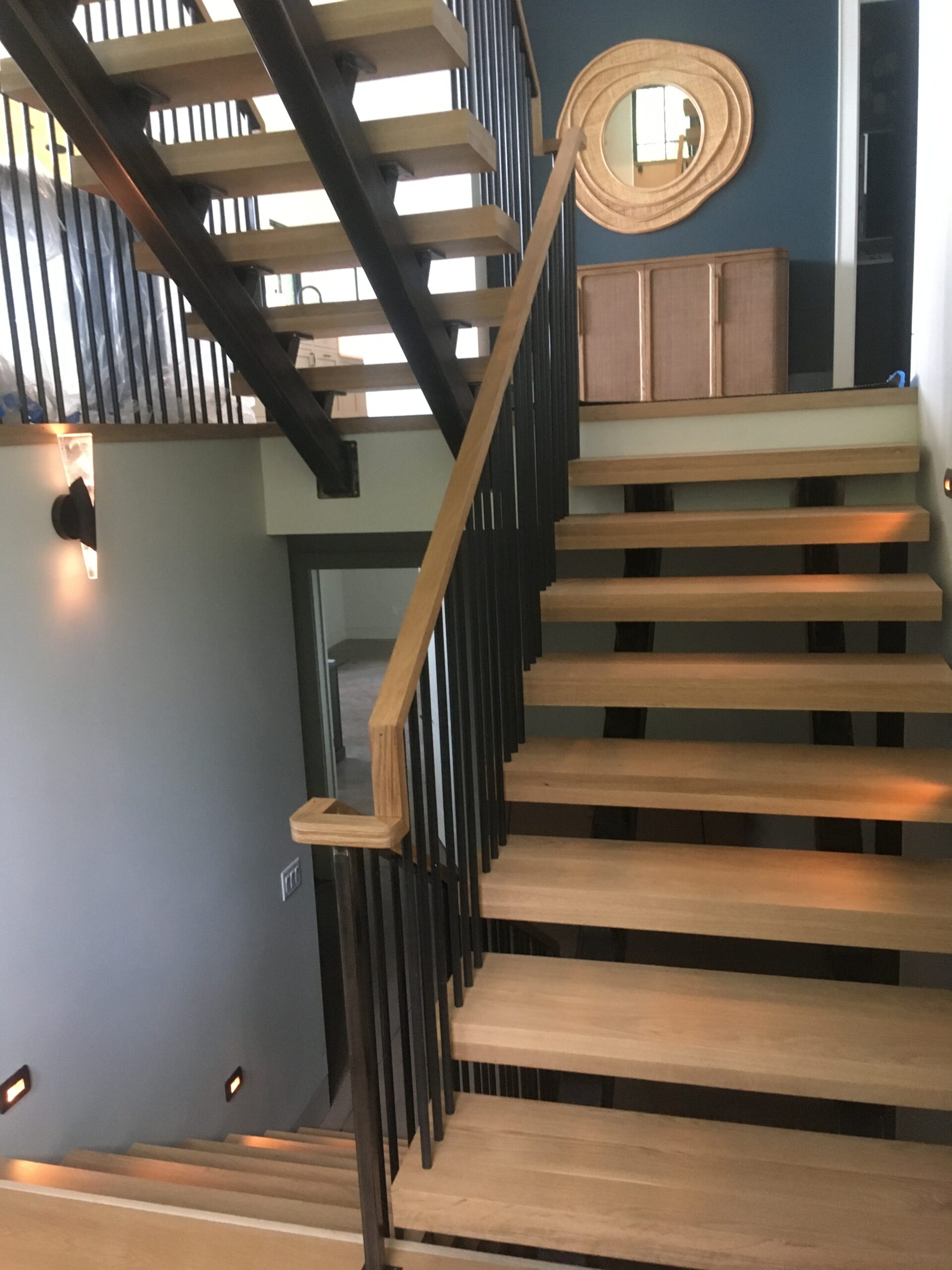 Open-riser staircase with black metal balusters, wood treads and a wood handrail