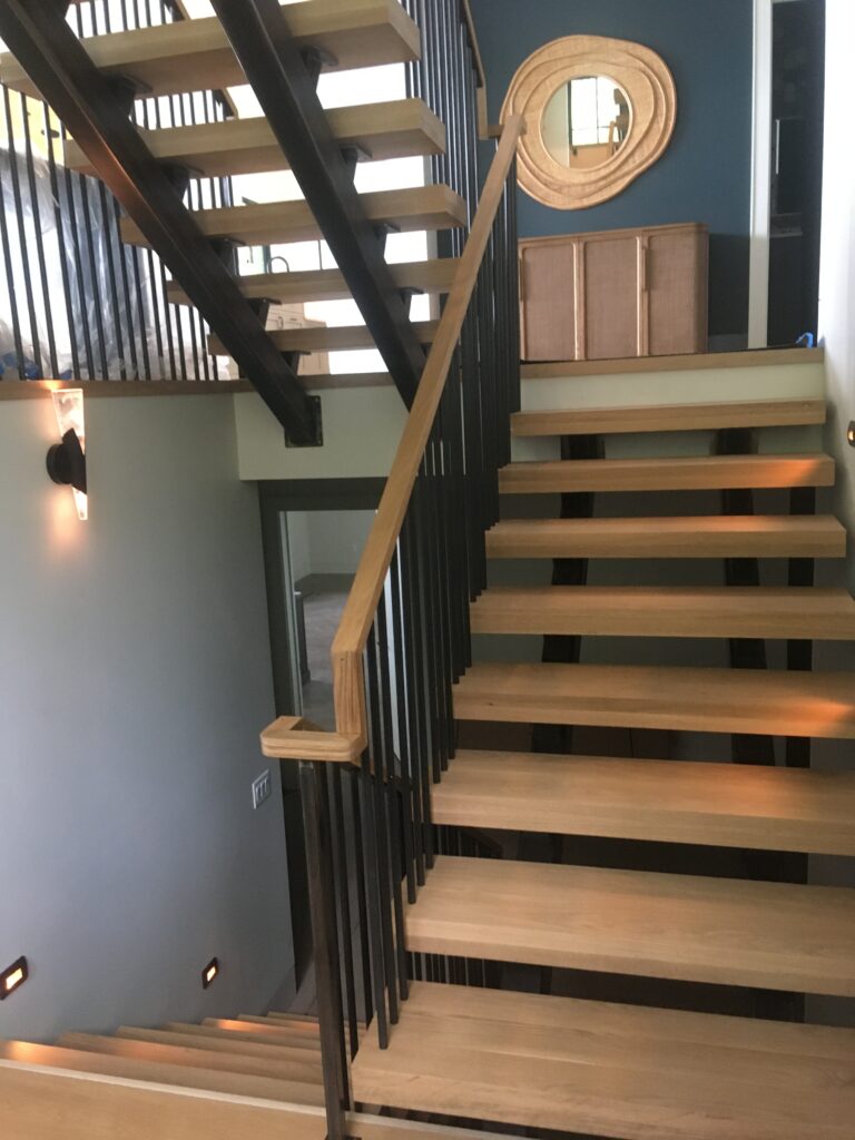 Open-riser staircase with black metal balusters, wood treads and a wood handrail