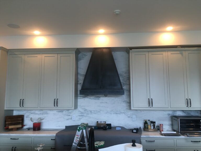 Blackened stainless steel range hood in a kitchen with white cabinets and a stone backsplash