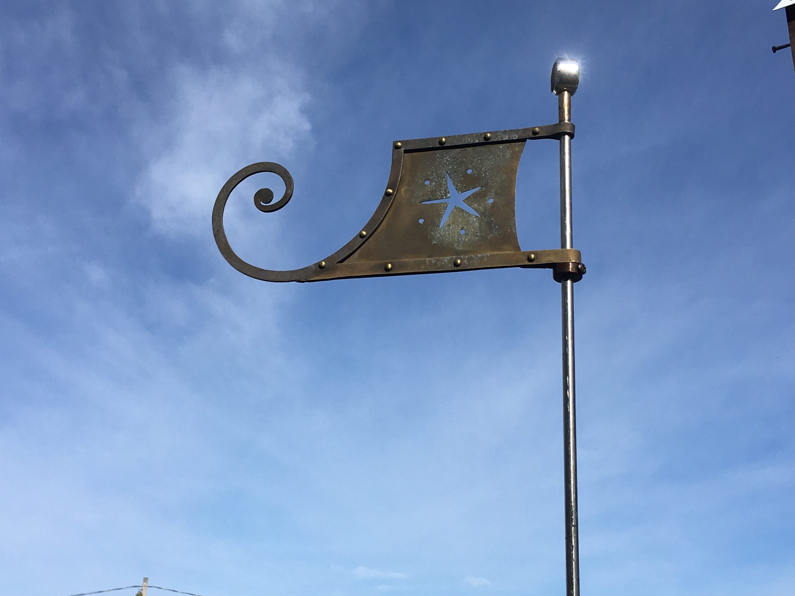 Bronze flag finial with a scrolled edge and a star cutout against a blue sky