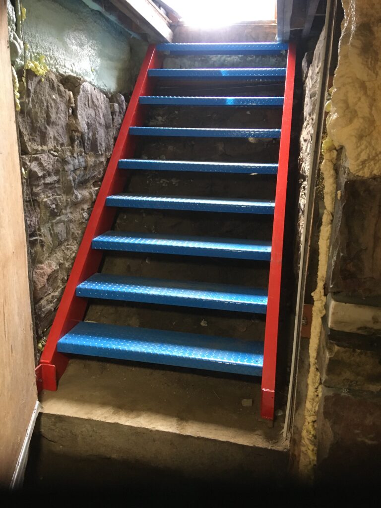 Steel bulkhead stairs with red stringers and blue treads between stone walls
