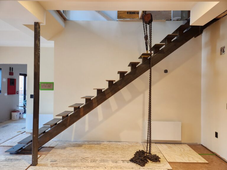 Open-tread staircase on a single central steel stringer in an unfinished room