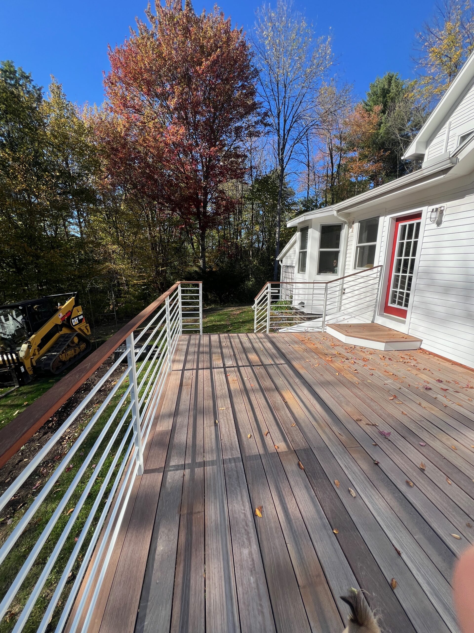 Horizontal-rod guardrail along a long wood deck beside a house in autumn