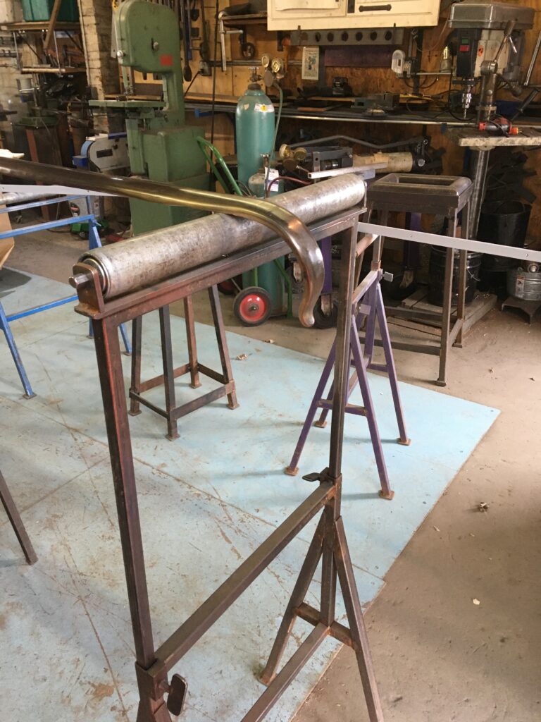 Long metal cap rail stock on roller stands in a metalworking shop