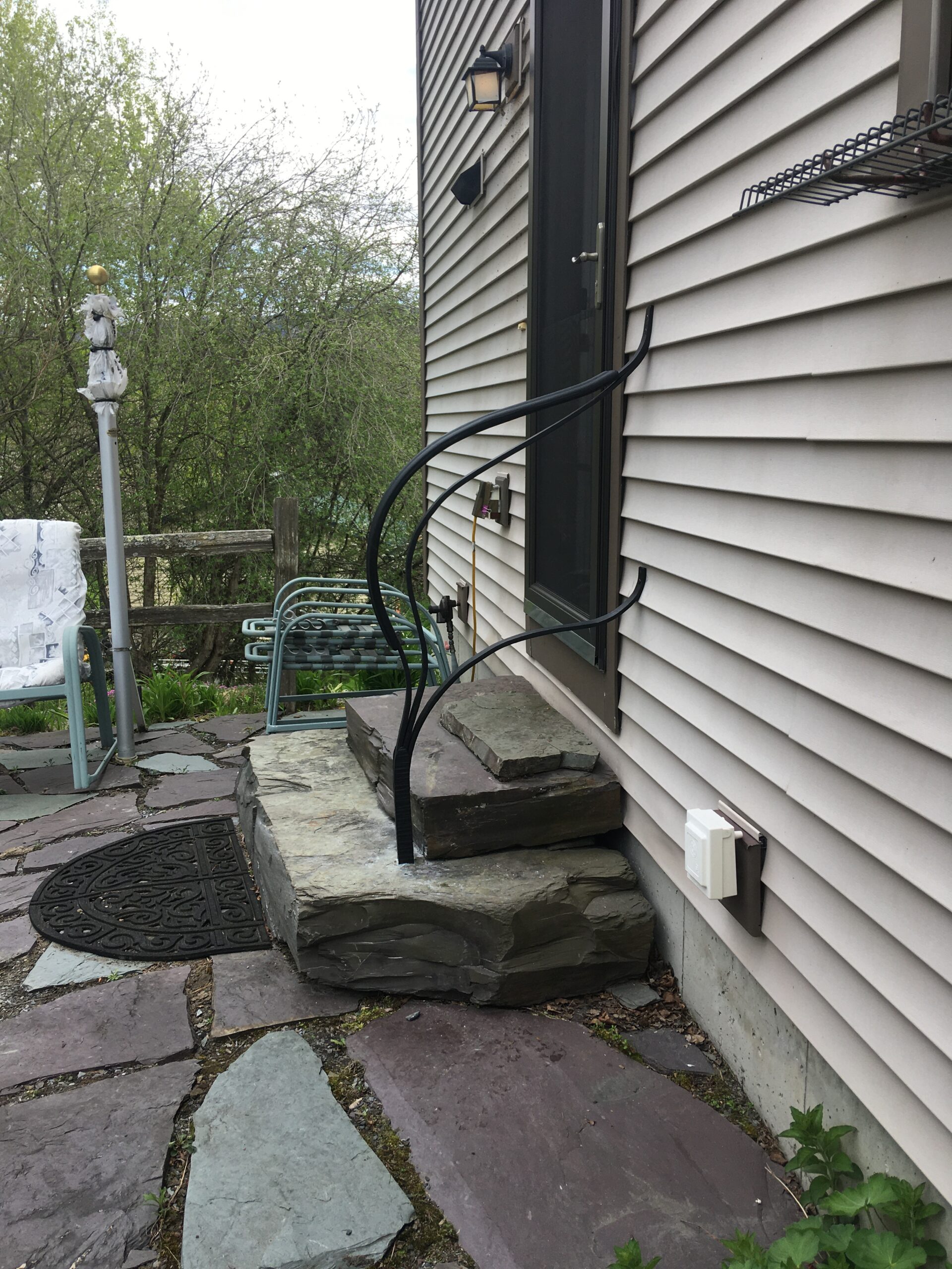 Curved forged metal rail beside stone steps at a house entry