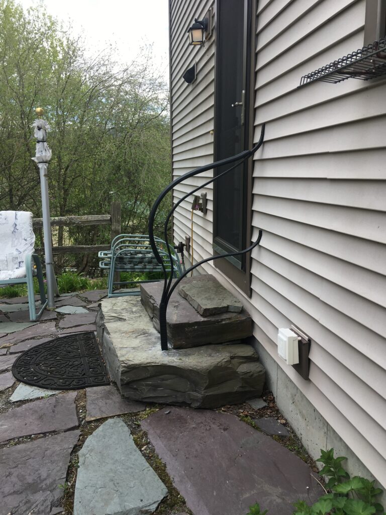 Curved forged metal rail beside stone steps at a house entry