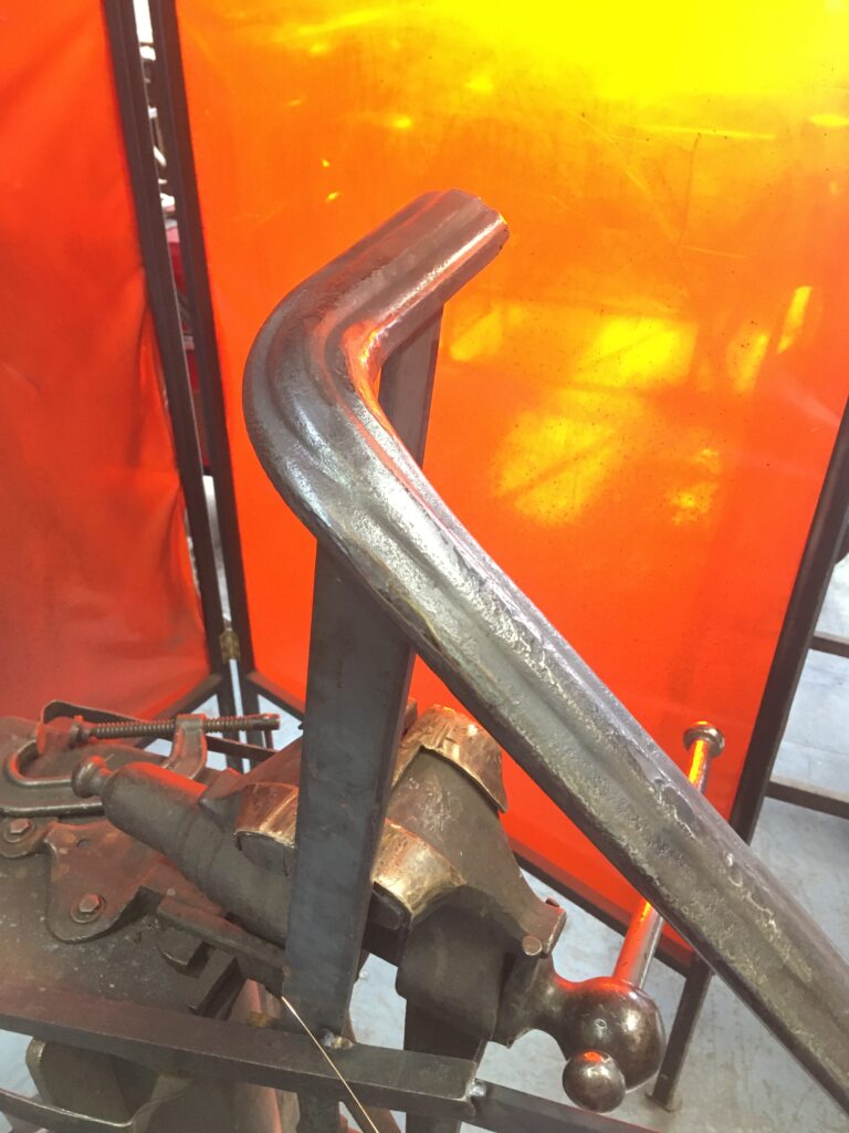 Bent metal rail section being formed beside a shop vise