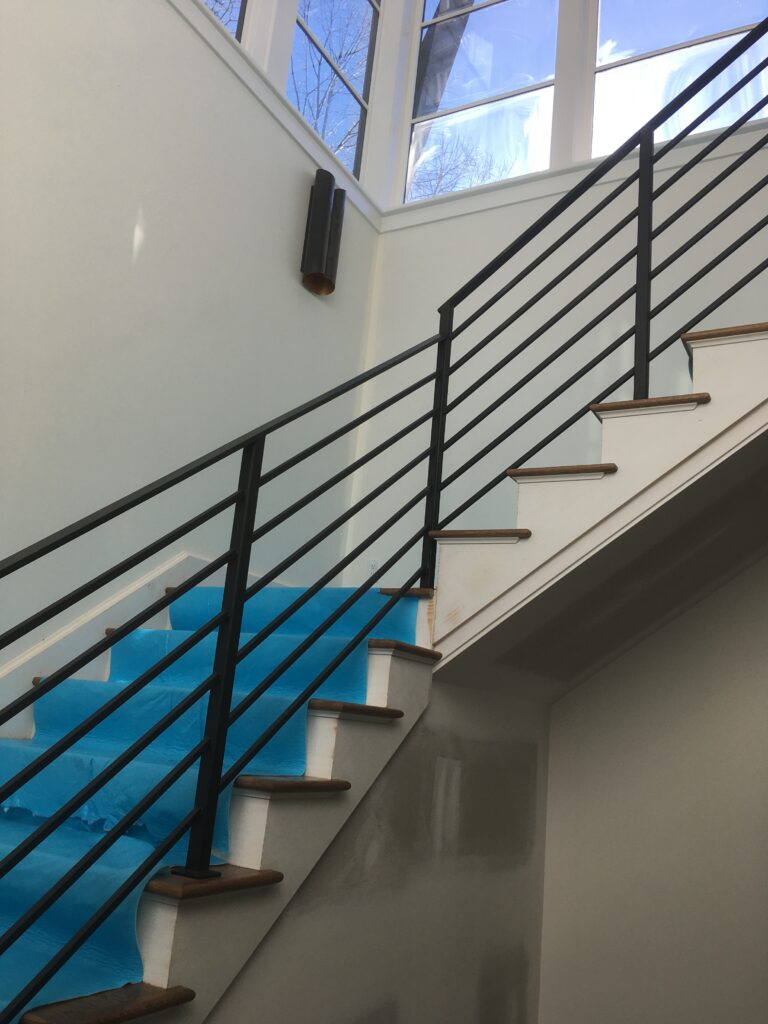 Black horizontal baluster railing on a staircase below tall windows