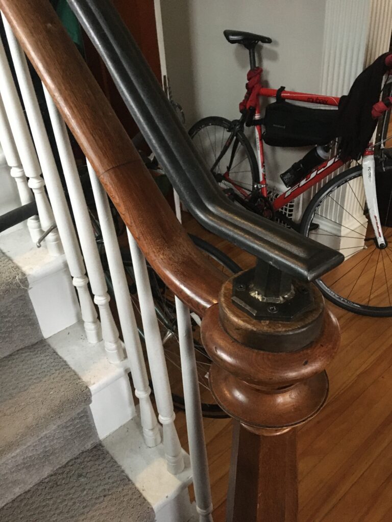 Wood handrail with a metal rail section above white balusters and a turned wood newel