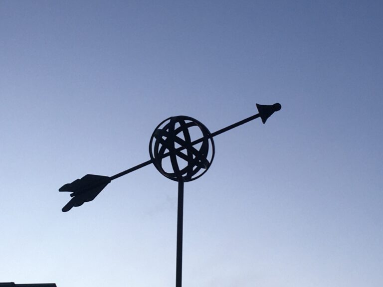 Silhouette of an orb-and-arrow finial against a dusk sky
