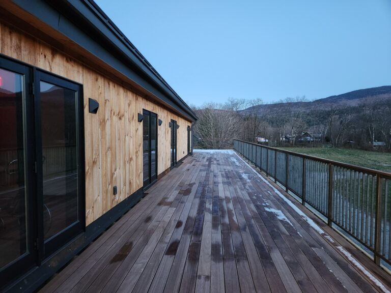 Dark metal railing running the length of a wood deck at dusk with hills beyond