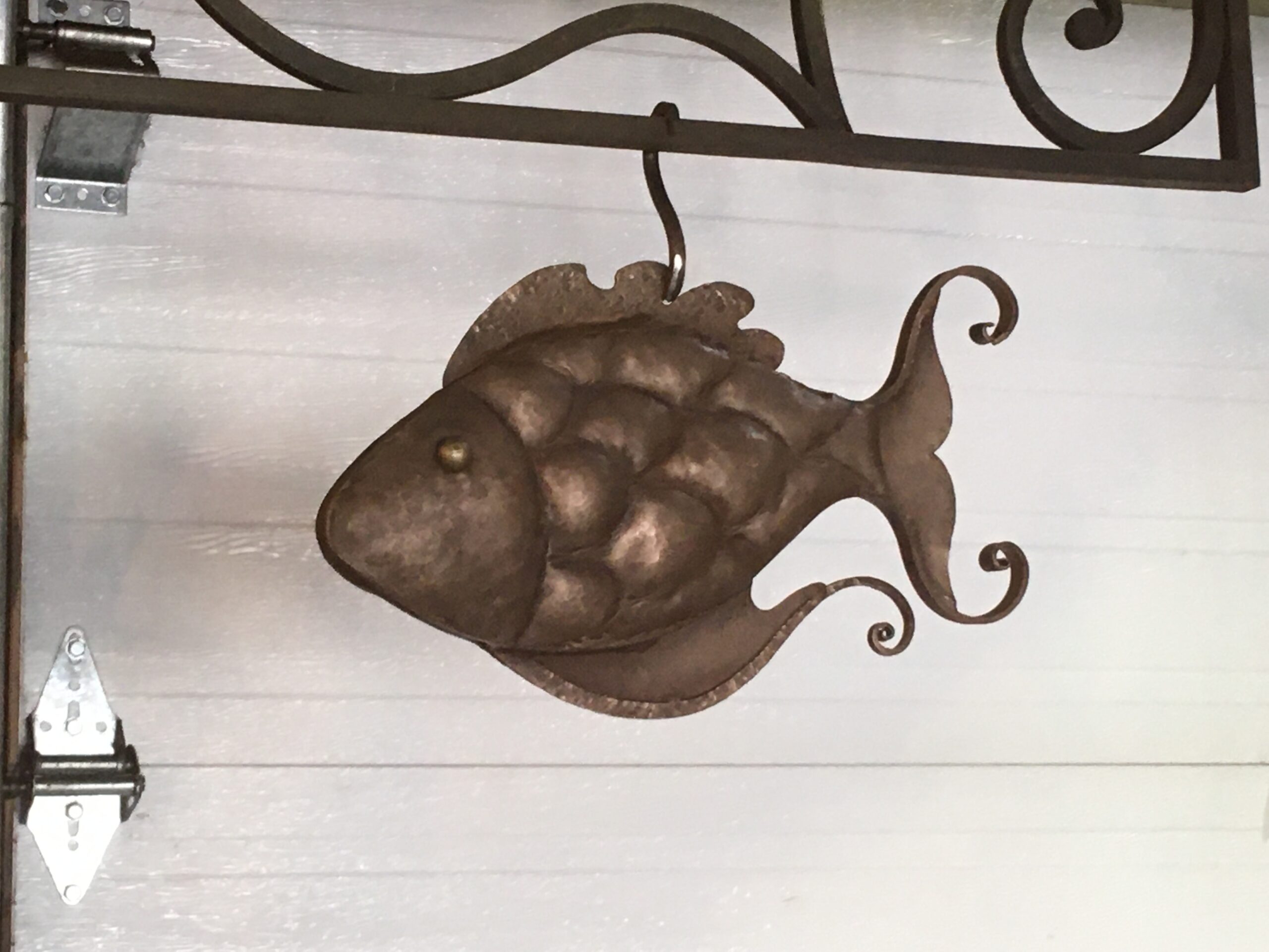 Hand-formed repoussé metal fish hanging from a scrolled metal bracket