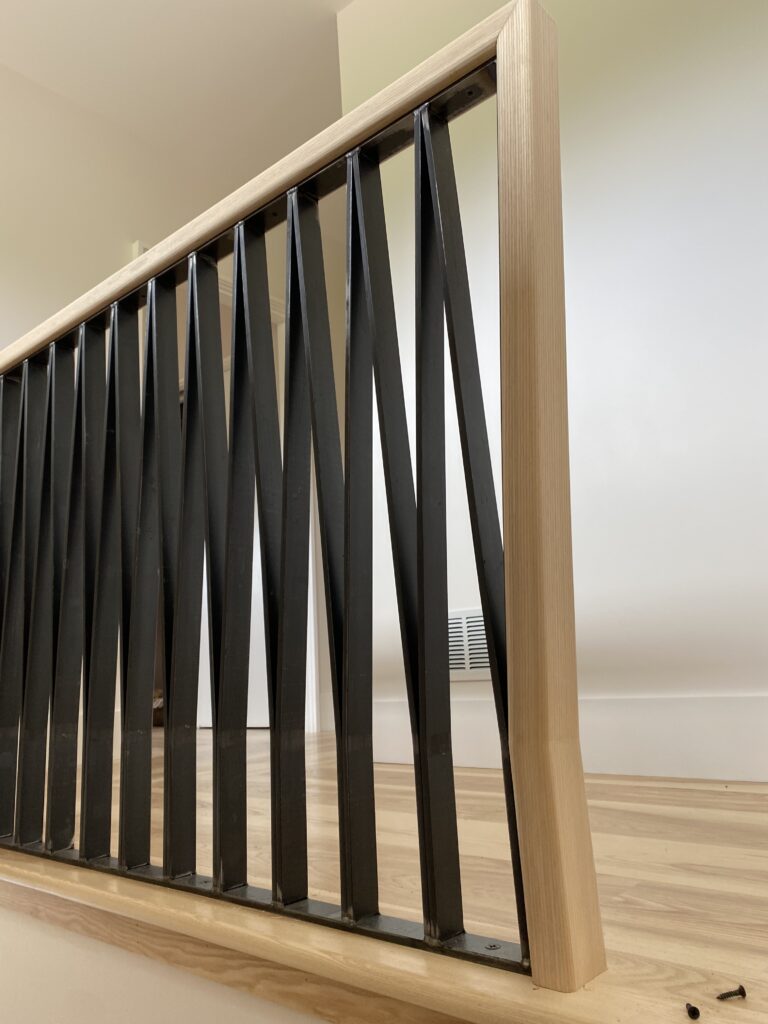 Black metal zigzag balusters with a light wood cap rail on an interior stair landing