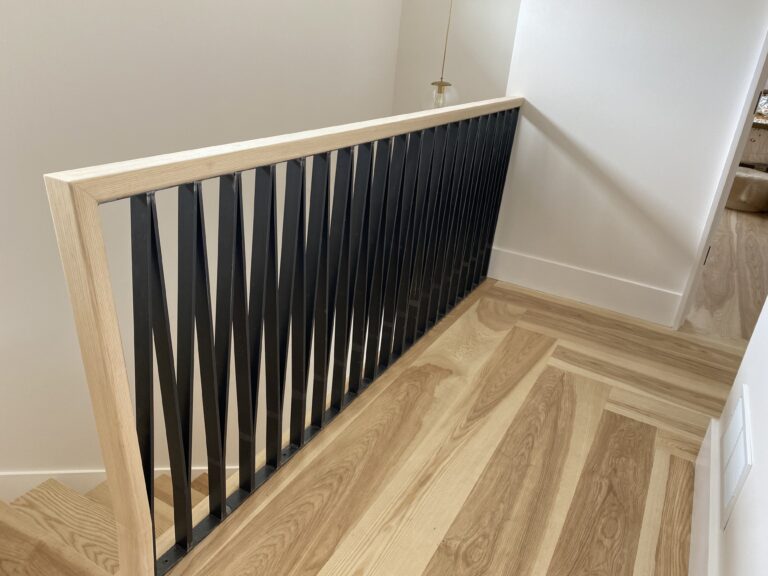 Black zigzag baluster railing with a wood cap beside a light wood floor